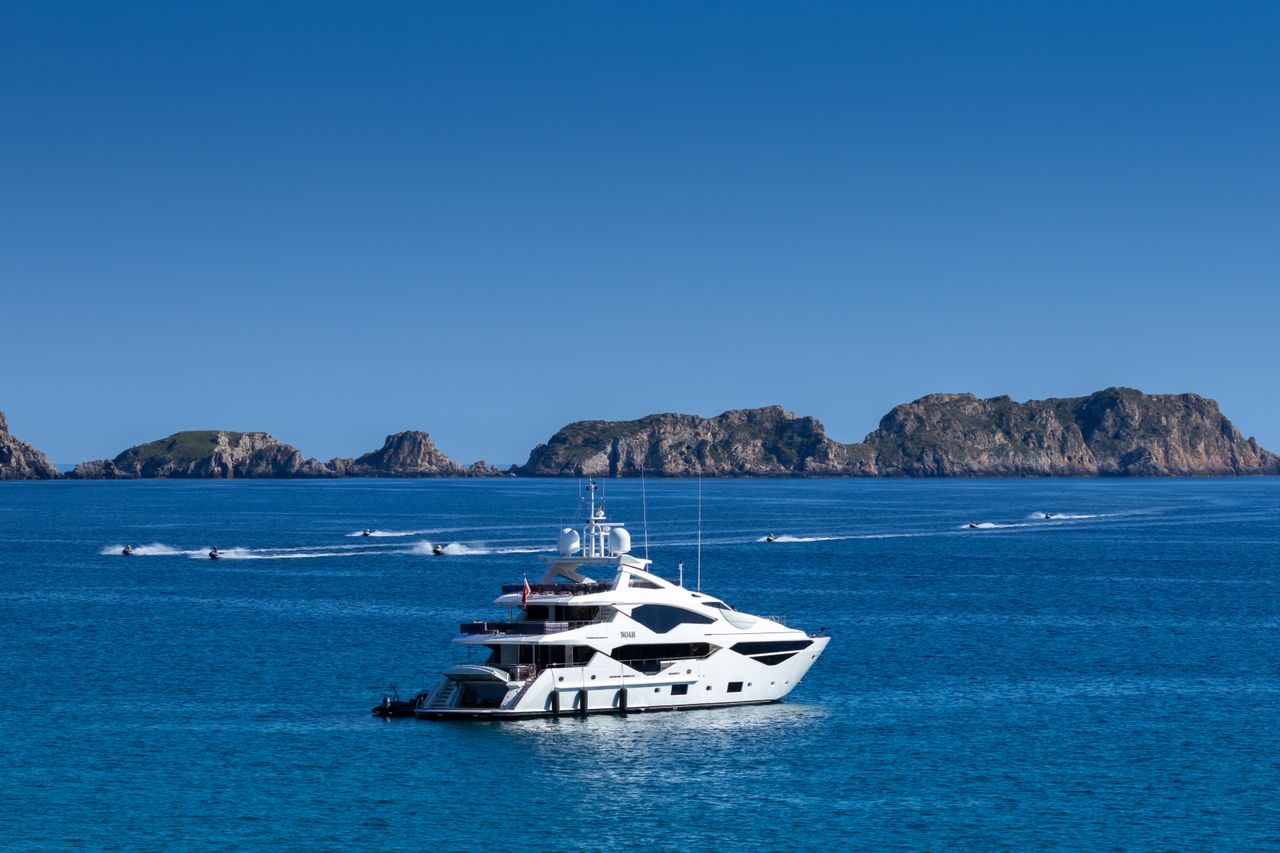 Luxury yacht in serene blue sea with scenic Spanish islands in background.